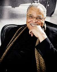 Man sitting with a black knit shirt and gold medallion