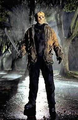 Ken Kirzinger as Jason Voorhees, A man wearing a hockey goalie mask and holding a machete stands in a road at night. The scene is back-lit.