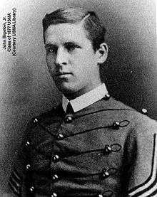 A black and white picture of John Bigelow, Jr., a young white male in his United States Military Academy Cadet uniform. His Cadet uniform has a starched white collar and his tunic has large round brass buttons interconnected by hortizontal braiding. He is clean shaven with neatly combed short dark hair parted to his right. His right sleeve shows two stripes indicating he is a Cadet Lieutenant.