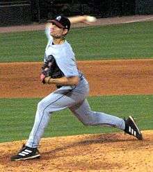 A man in a gray baseball uniform and black cap prepares to throw a baseball from his right hand as he stands on the pitcher's mound.