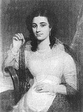 A dark-haired, exotic-looking young lady in a light-coloured dress.