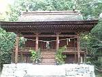 Small wooden building with a curved roof and stairs leading to a platform surrounding the building.