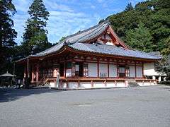 Wooden building with raised floor, white walls, vermillion red beams, an open veranda and a hip-and-gable roof.