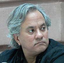 Headshot of an Indian man with gray hair and black shirt