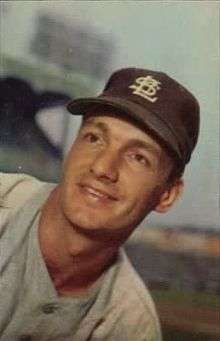 A man in a gray baseball uniform wears a dark cap with an overlapping "STL" on the center.