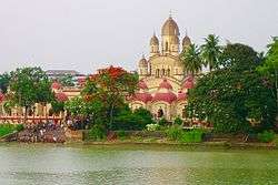 A temple with nine spires and few small temples surrounding it, with a waterbody in the foreground