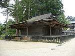 Wooden building with a hip-and-gable roof and step canopy. A shorter aisle is attached to the right side.