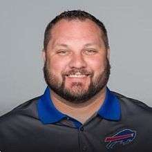 Posed head and shoulders photograph of Anderson with a beard wearing a grey Buffalo Bills polo shirt