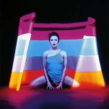 Minogue in a blue mini dress, inside of a fluorescent multi-coloured cut cone.