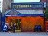 A brick building with an entrance below a sign reading "LADBROKE GROVE STATION". Three people are in a group ouside the entrance