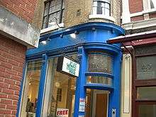 A building painted blue, with a sign reading "The Glass House". An advertisement on glasses is affixed on the door.