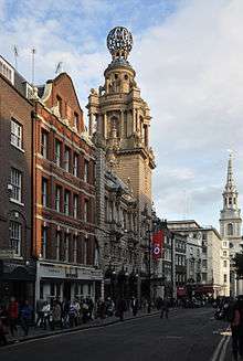 An Edwardian theatre stands as part of a row of buildings. It has a tower topped by a globe. A banner with the letters ENO hangs above the entrance.