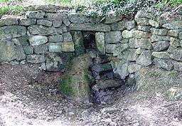 a very small stream issuing from an opening in a stone wall.