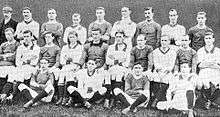 A black and white photograph of a football team in alternating light and dark shirts