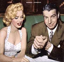 Monroe wearing a white polka-dot dress and sitting next to Joe DiMaggio in a restaurant-type setting