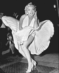 Monroe is posing for photographers, wearing a white halterneck dress, which hem is blown up by air from a subway grate on which she is standing.