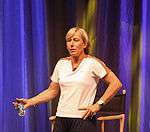 A woman, with a white shirt and black shorts is standing up