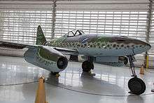 A color photo of a twin engine jet-fighter aircraft standing in a hangar.