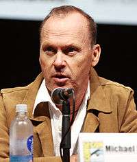 A close-up of a man wearing a white shirt underneath a beige coat at a conference.