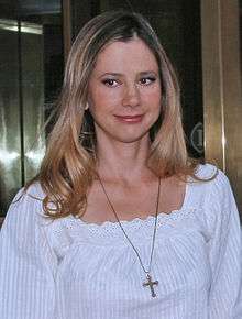 Profile of a blonde woman who is wearing a religious necklace over a white dress.