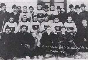 Several rows of men, some wearing hockey uniforms, the others in overcoats and top hats.