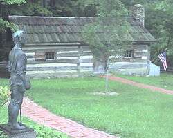 A log cabin with a statue and a tree in front