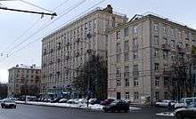 Large gray multi-story building, with trees and cars parked in front