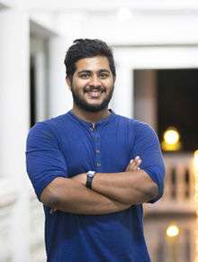 A photo of Navaneeth Unnikrishnan standing with crossed-arms in a blue t-shirt