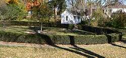 One-room building with small porch; circular hedge about 100 feet in diameter