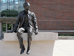 Photo of a statue of Neil Armstrong sitting on a ledge. The words "Neil Armstrong Hall of Engineering" are visible on the building in the background.