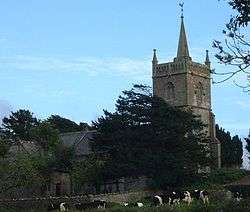 Gray stone building with tower at right hand end surmounted by a small spirelet, partially obscured by trees.