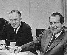 Two middle-aged men sit at the right side of a large tabletop.