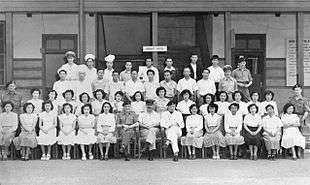 Four rows of people, mostly in civilian clothes, some in military dress, in front of a building marked "Transit Hotel"