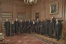 Nine judges in black robes pose for a photograph with three other men in suits.