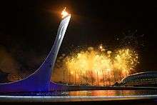 The tower with flame at the top. The background is sky with fireworks.