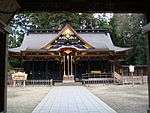 Wooden building with a large roof and central gable on the front. Both the roof and the lower part are in very dark colors. Three ropes are hanging down from the front centre gable.