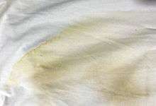 A yellow stain, pronounced at its sharp upper boundary and lighter further down, on white cloth