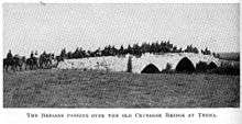 Photo shows brigade crossing the three arched stone bridge (two smaller arches on either side of a central larger arch) with the road grading up to the center and down on the ends.