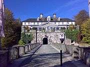 At the end of a bridge over a moat, a grand castle surrounded by trees