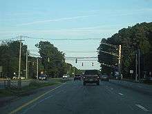 Ground-level view of a four-lane divided highway with a narrow grassy median separating the opposing lanes of traffic; a traffic signal is visible in the distance