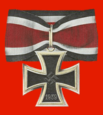 A silver framed black cross that has arms which are narrow at the center, and broader at the perimeter. In the middle of the cross is a swastika, an equilateral cross with its arms bent at right angles. On the lower arm of the cross are the number 1939 engraved. The cross is connected to a ribbon with a silver clip. The ribbon has a red central stripe, flanked in white and with a black edge stripe.