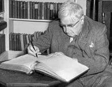 Old man, with white hair, seated at a desk, writing