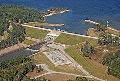 A dam in front of a large lake in between two groups of trees