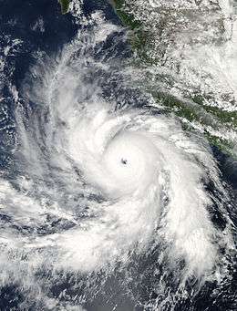 Visible satellite image of a powerful, mature hurricane near the western coast of Mexico. The storm features a well-defined, clear eye surrounded by a large mass of intense convection. Rotating feeder bands, curving into the system, are present around the entire hurricane.