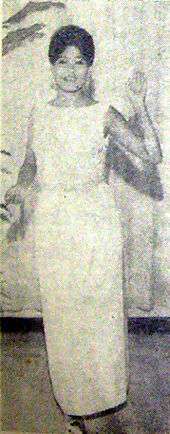 A black and white photograph of a woman in a party dress looking forward.