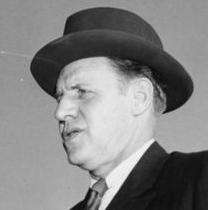 3/4 view of white man with dark hair, slightly fleshy face, necktie, dark suit, dark homburg