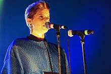 Robyn singing on a dark stage, in front of two microphones