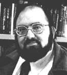 Black and white head shot of a bearded man wearing glasses