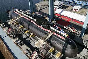 Aerial photograph of a submarine removed from the water in a dock, flags and banners decorate the submarine.