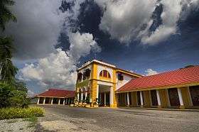 A large two storey building with two wings, painted yellow and white with a red tiled roof